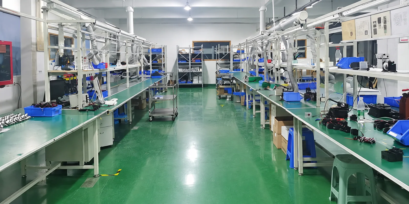 Assembly workshop with green workbenches, component trays and electronic instruments